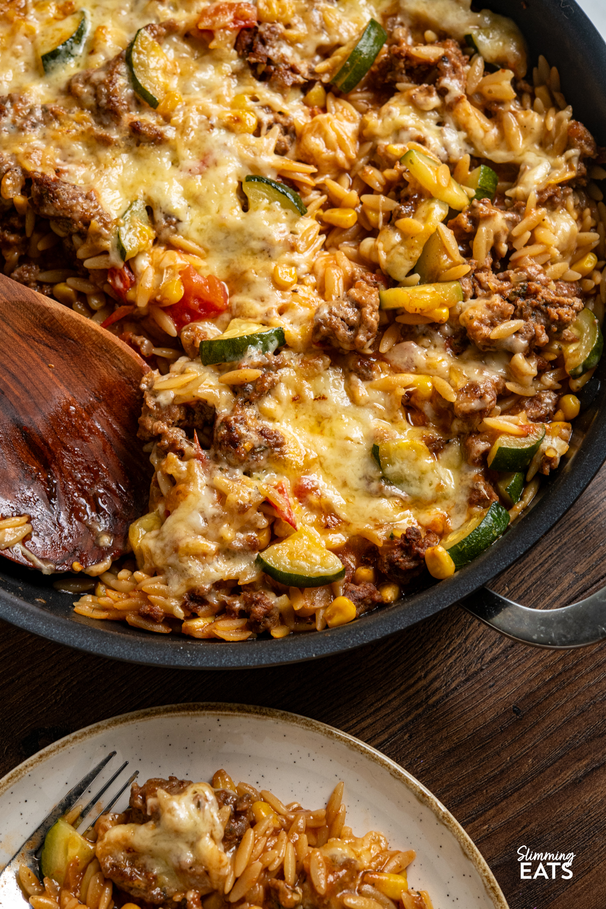 close up of One Pan Cheesy Ground Chicken Orzo with Zucchini and Corn in double handled non stick pan with wooden spoon