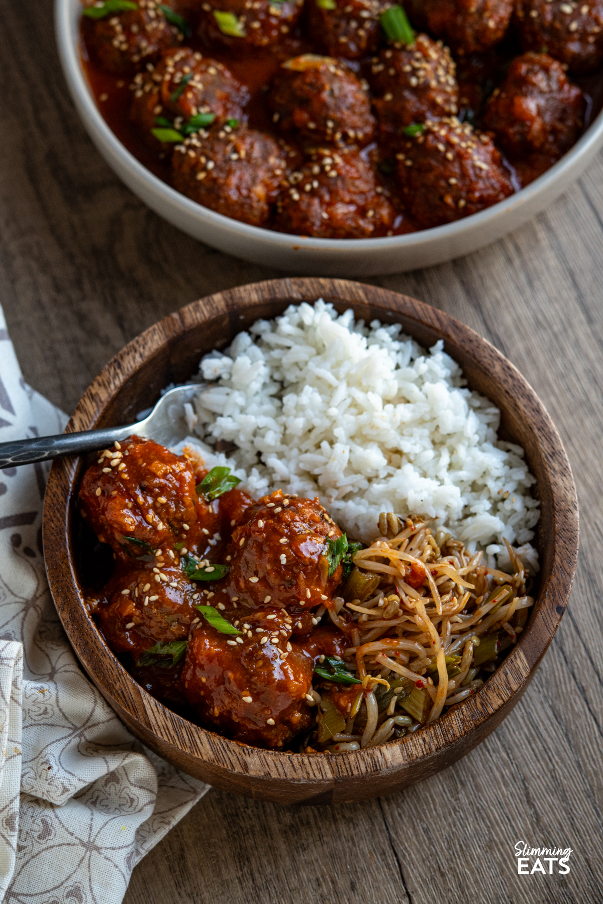 pork meatballs in gochujang pineapple sauce in a wooden bowl with white rice, fork placed in left hand side of bowl, beige bowl with remaining meatballs above