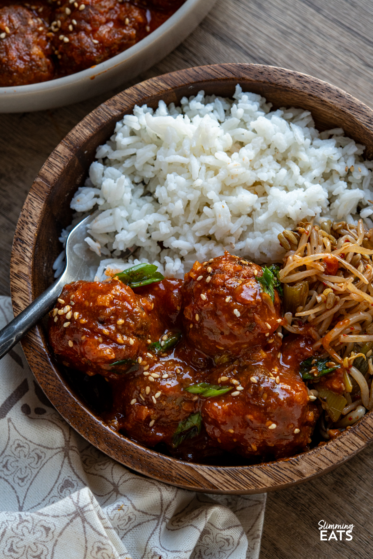 pork meatballs in gochujang pineapple sauce in a wooden bowl with white rice, fork placed in left hand side of bowl, beige bowl with remaining meatballs above