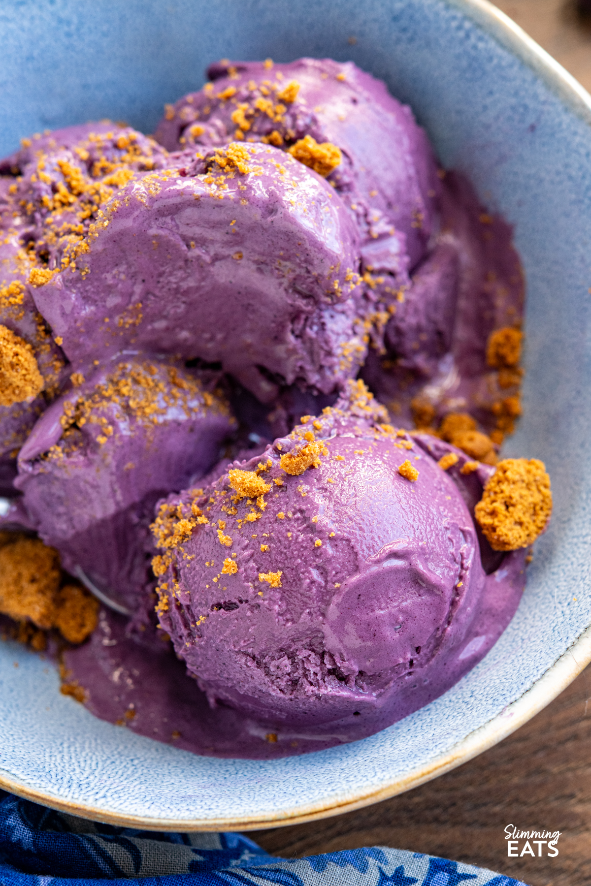 Blueberry Banana Frozen Yoghurt in a blue bowl with spoon topped with crumbled lotus cookie