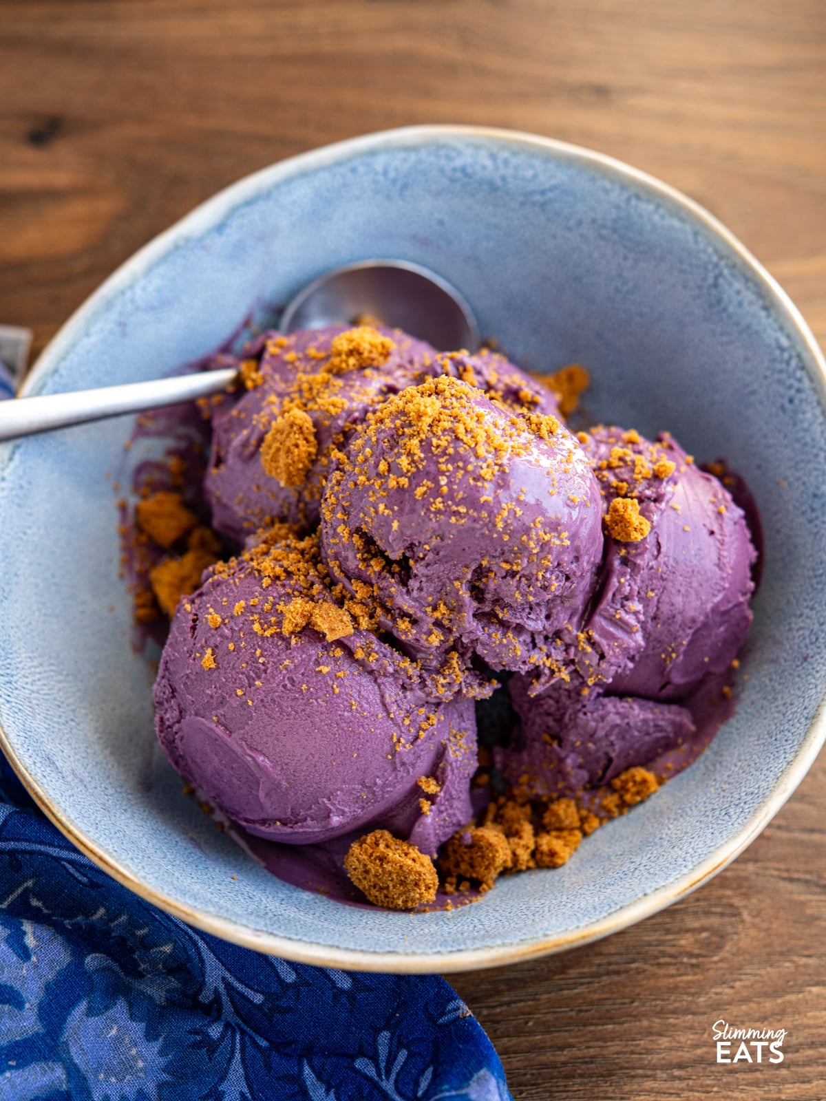 Blueberry Banana Frozen Yoghurt in a blue bowl with spoon topped with crumbled lotus cookie